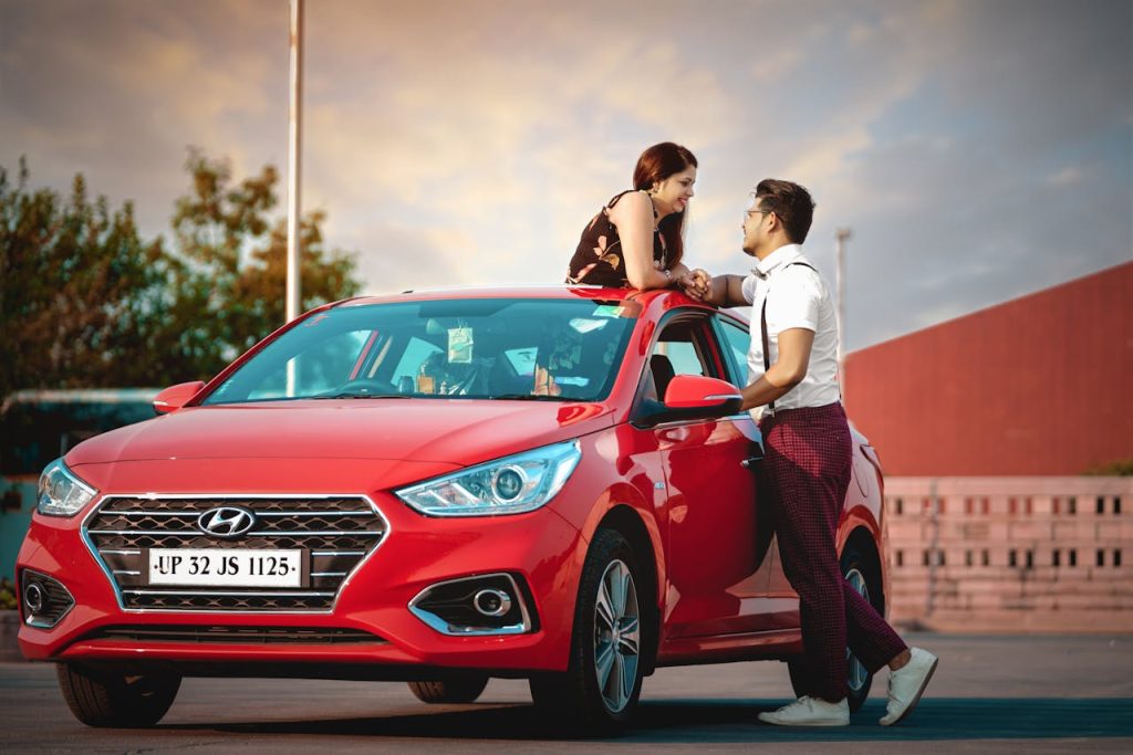 A young couple shares a moment by a red car, capturing love and modern lifestyle in Delhis vibrant outdoor setting.